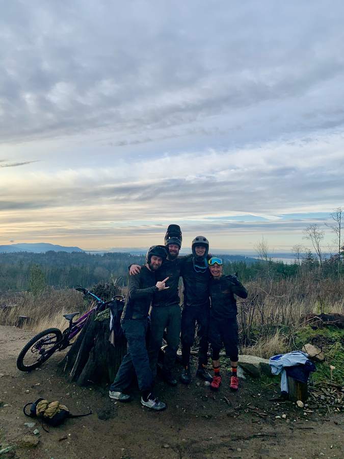 Four muddy riders all smiles at golden hour above the bay