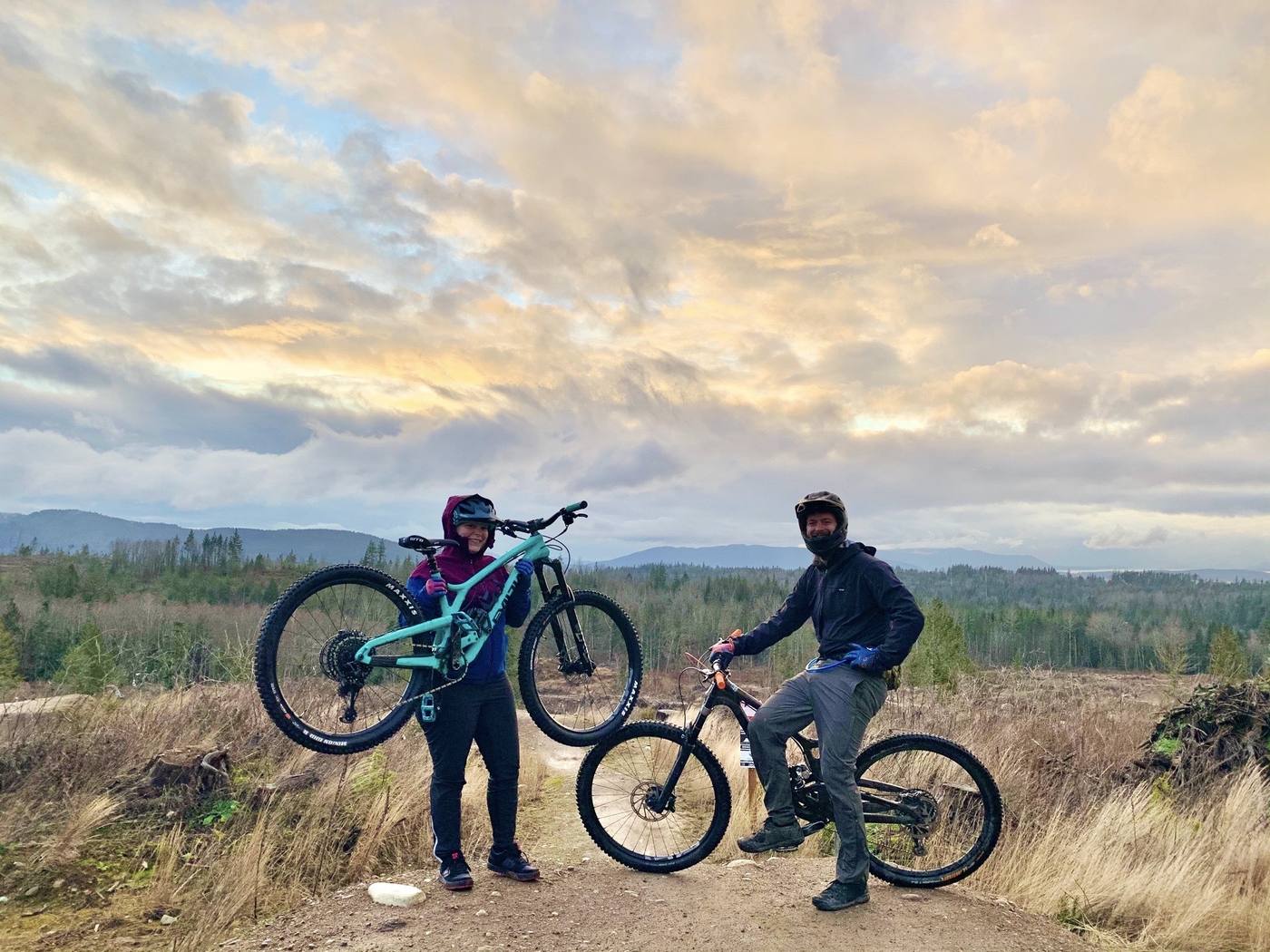 Two Send It Society riders with their bikes at golden hour above the valley
